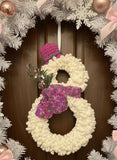 Two white wreaths with pink and purple knitted mittens on a black textured background