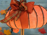 A 3D fabric wreath decorated with orange and with a plaid ribbon, designed to resemble a pumpkin.