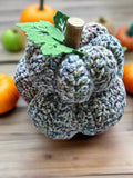 Knitted pumpkin decoration on a wooden surface with other pumpkins in the background