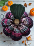 Knitted pumpkin decoration with a real acorn on a wooden surface with small pumpkins and leaves.